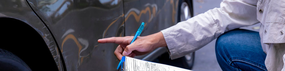 Insurance Agent Writing On Clipboard While Examining Car After